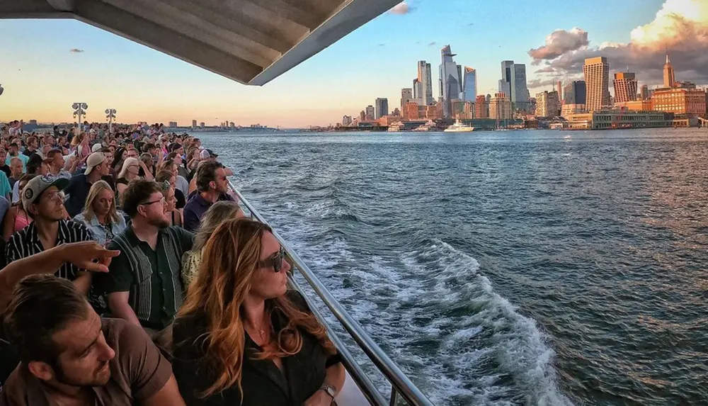 A group of passengers enjoys the view from a boat as it cruises near a city skyline at sunset
