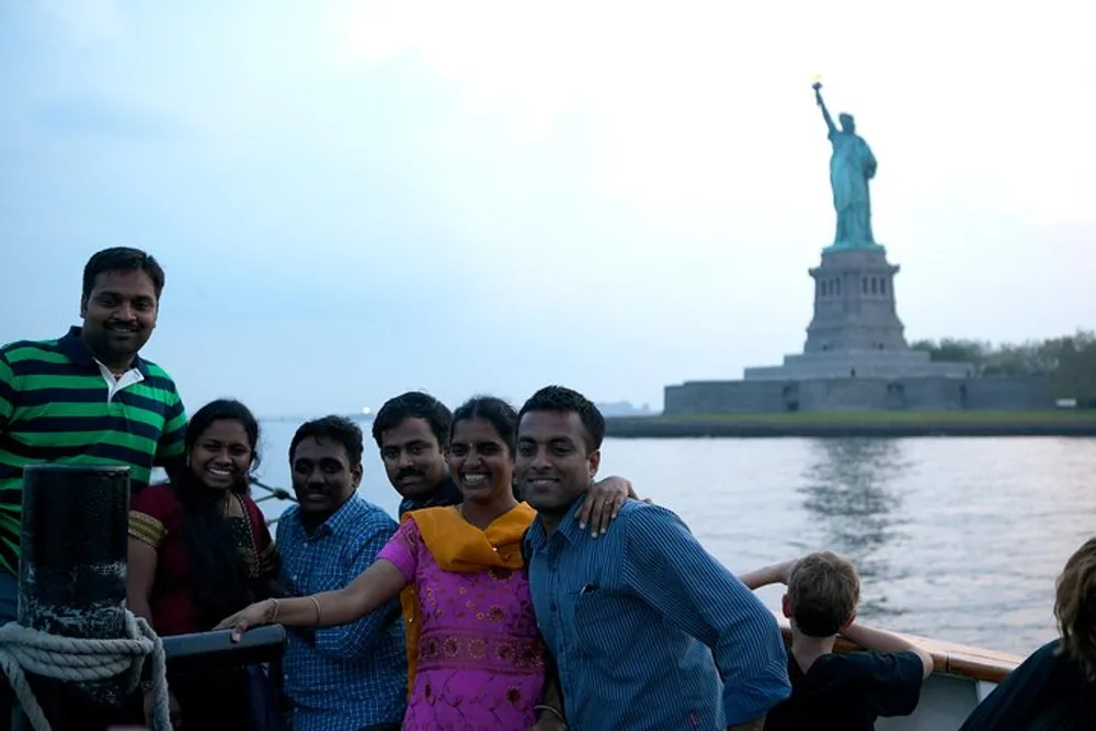 A group of smiling people are posing for a photo on a boat with the Statue of Liberty in the background