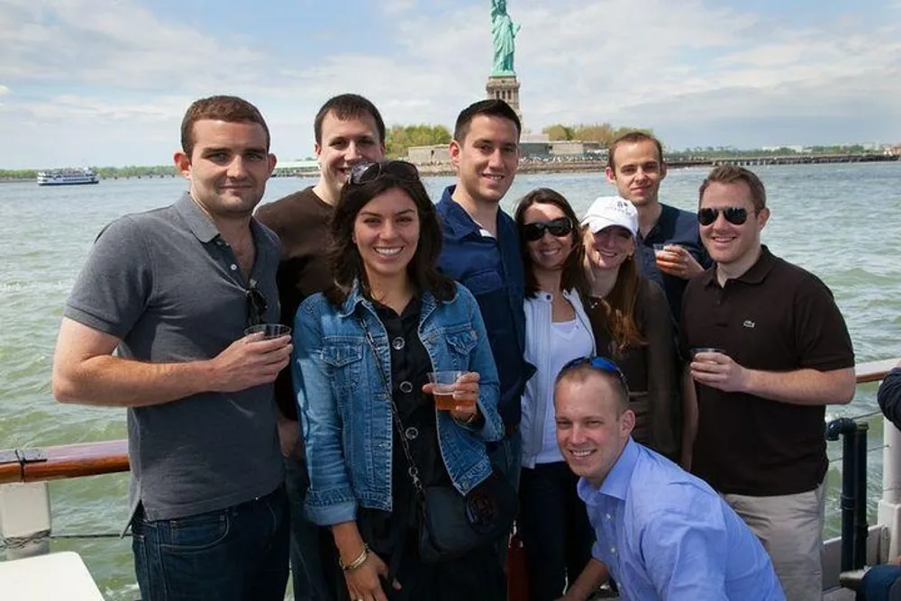 A group of people is smiling and posing for a photo on a boat with the Statue of Liberty in the background
