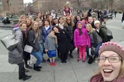 A group of smiling people of various ages are posing for a selfie, with one person in the foreground holding the camera and extending her arm to capture everyone.