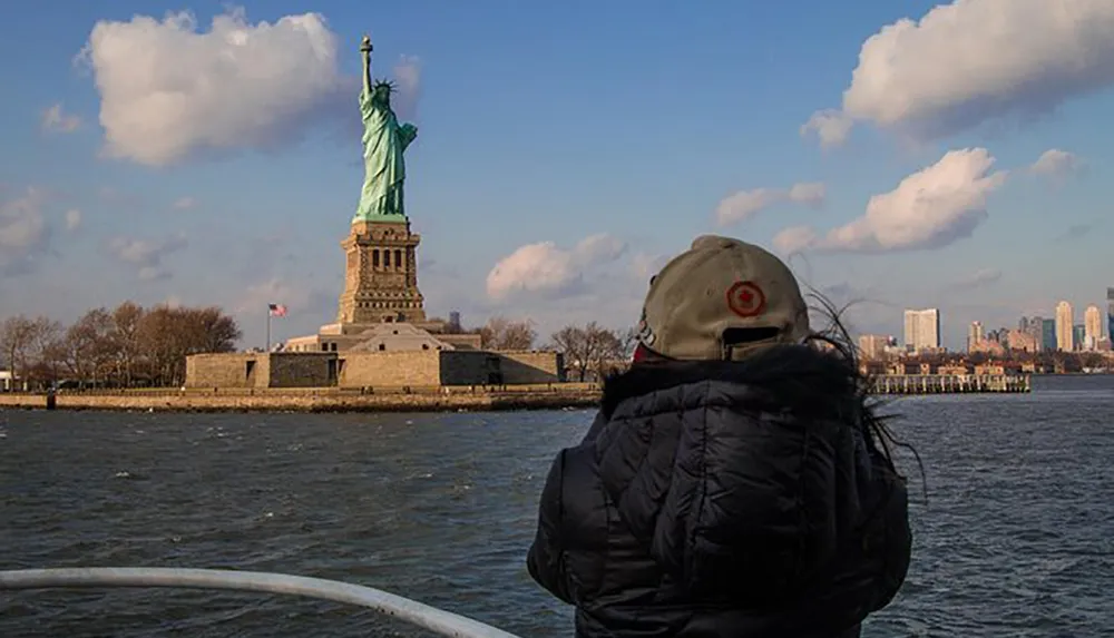 A person is gazing towards the Statue of Liberty from a boat on the water