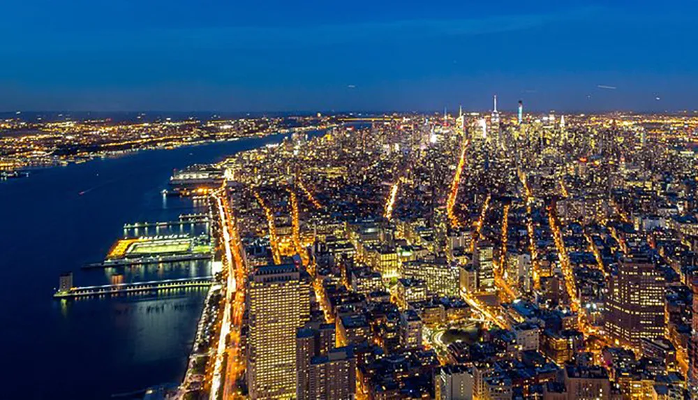 This image captures a bustling metropolitan area at dusk with an expansive view of a brightly lit city grid bodies of water and a vibrant skyline