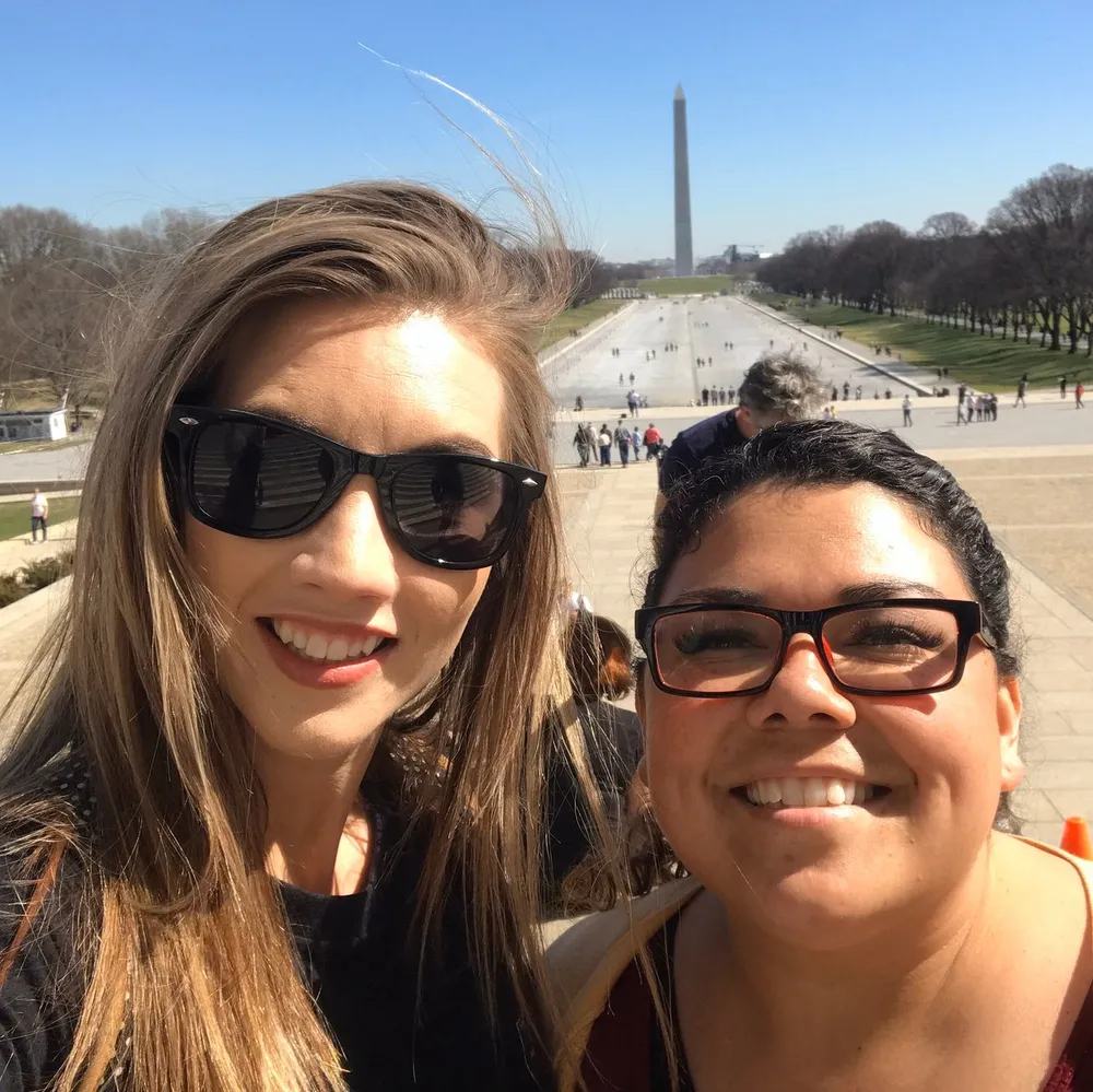 Two people are taking a selfie with the Washington Monument in the background