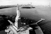 The image is a black and white aerial view of the Statue of Liberty with the New York City skyline in the background.