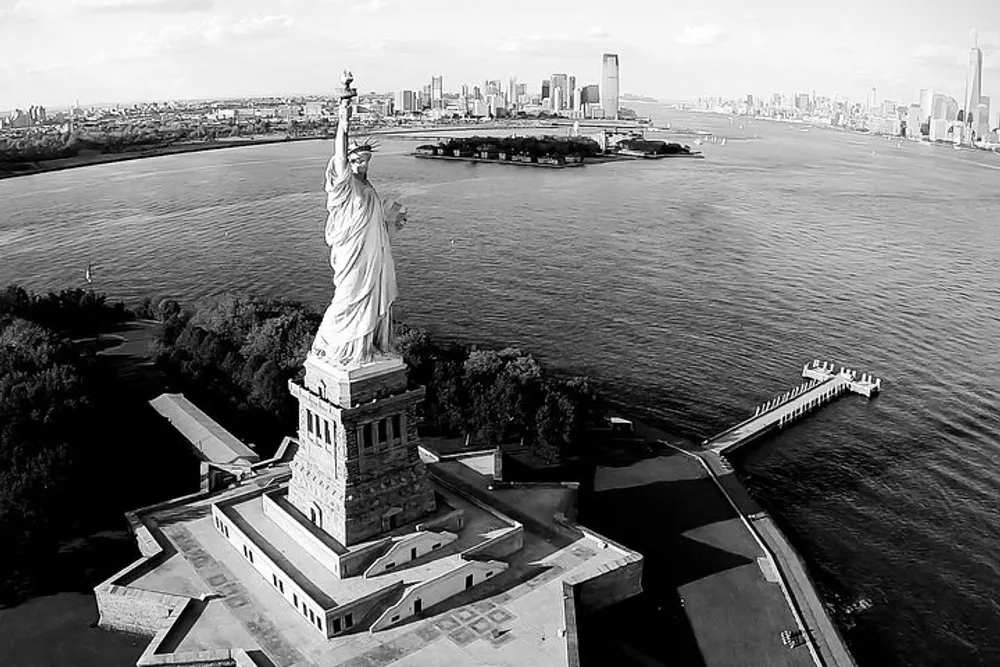 The image is a black and white aerial view of the Statue of Liberty with the New York City skyline in the background