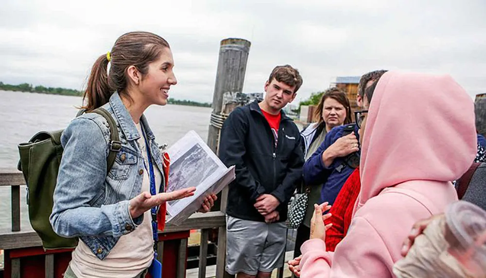 A smiling tour guide is engaging with a group of attentive listeners by a waterfront