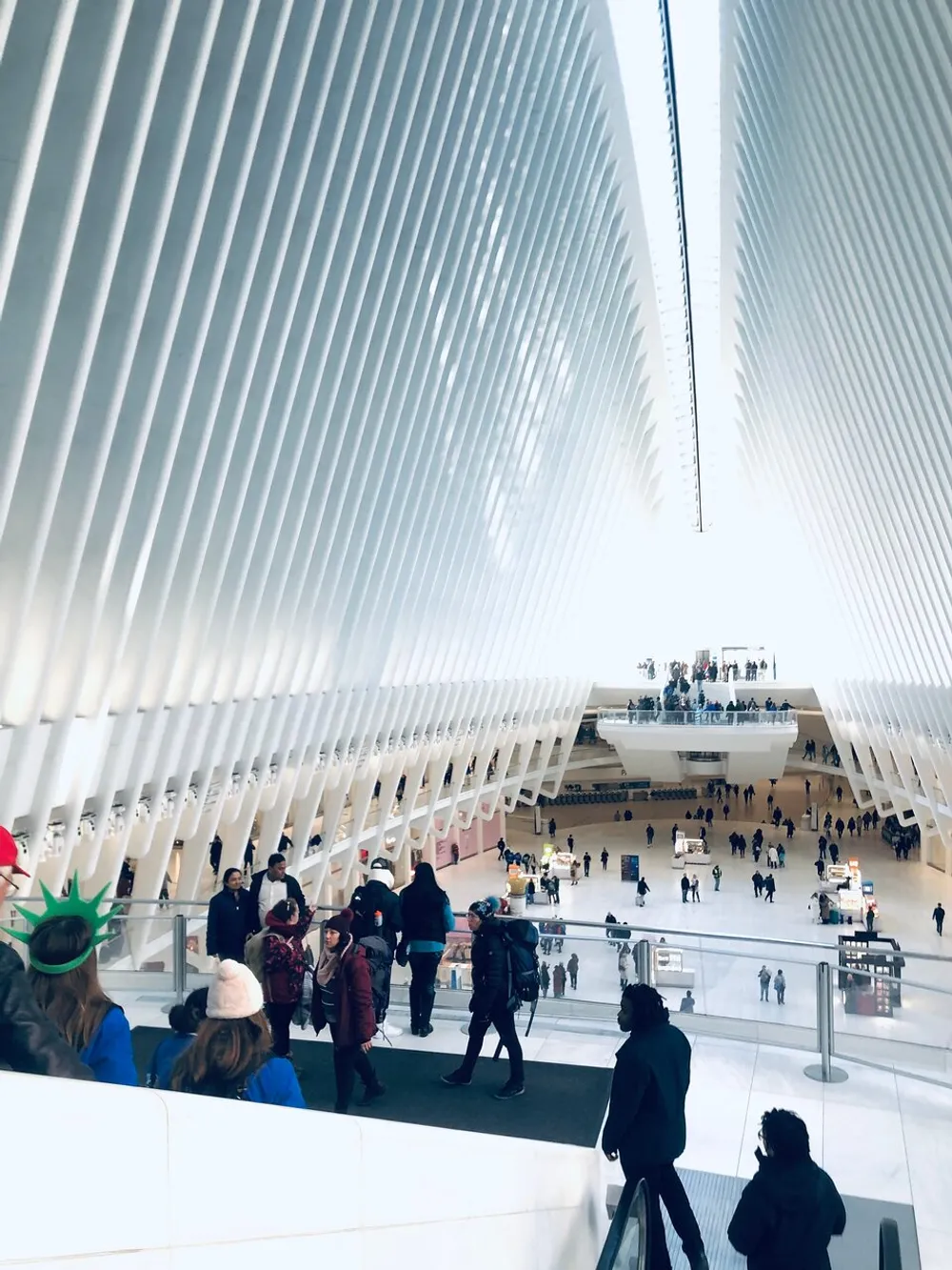 The image features a bustling interior view of the Oculus transportation hub in New York City displaying its distinctive white ribbed structure and people walking about