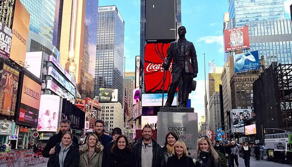 A group of people poses for a photo in bustling Times Square under the watchful gaze of the George M Cohan statue with vibrant electronic billboards illuminating the background