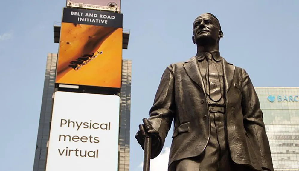 This image captures a statue of a standing figure in the foreground with a billboard advertising the Belt and Road Initiative and another sign proclaiming Physical meets virtual in the background