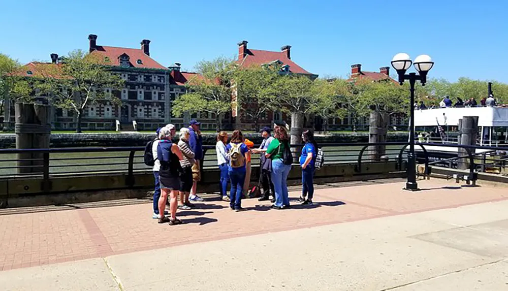 A group of people are gathered on a sunny day near a dock with some standing and having a conversation while a person in blue looks on