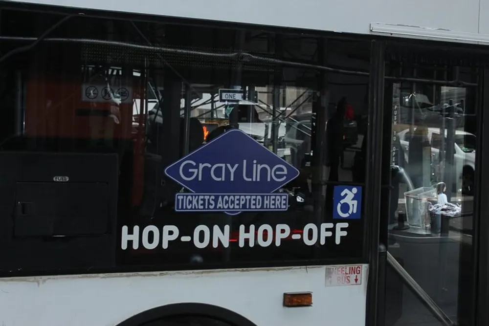 The image shows a section of a white Gray Line hop-on hop-off tourist bus with the companys signage and accessibility symbol displayed on its side