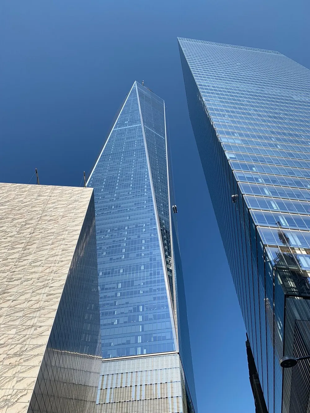 The image shows a worms-eye view of tall skyscrapers against a clear blue sky with one building reflecting the sky on its glass facade