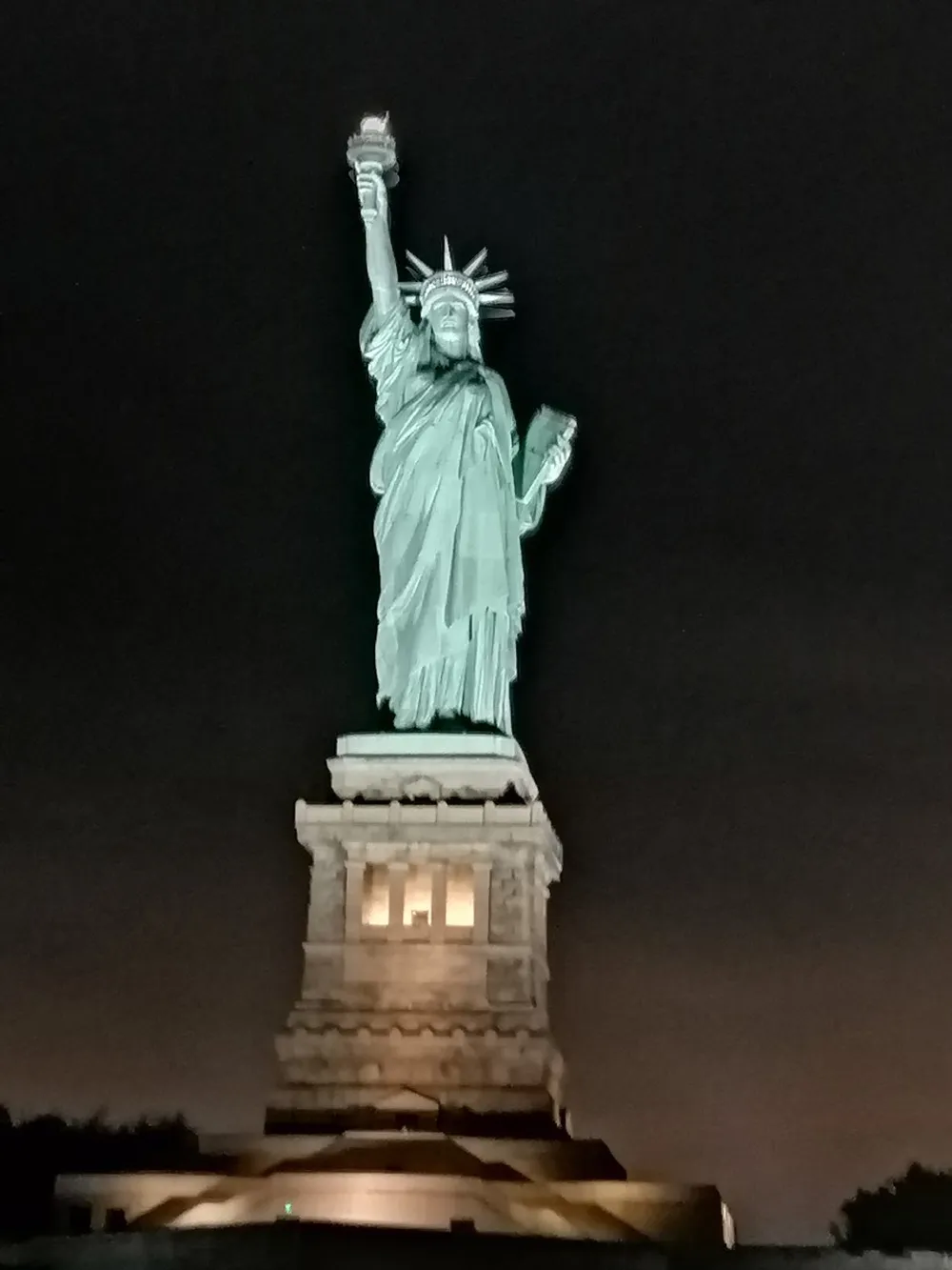 The image is a nighttime photo of the Statue of Liberty illuminated against a dark sky