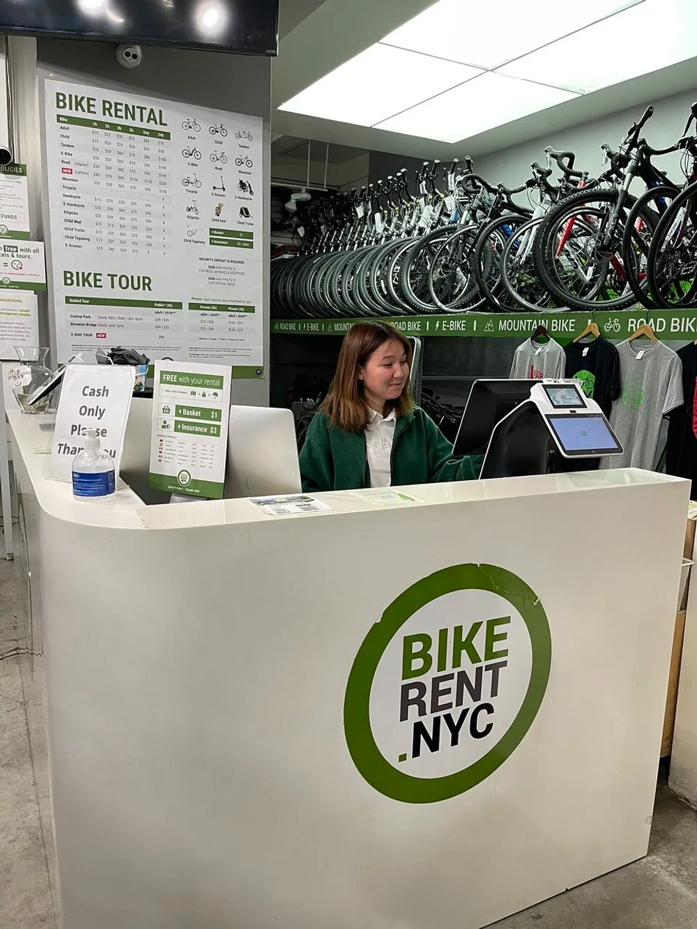 A person is seated behind the counter of a bike rental shop with information on bike rentals and tours visible in the background