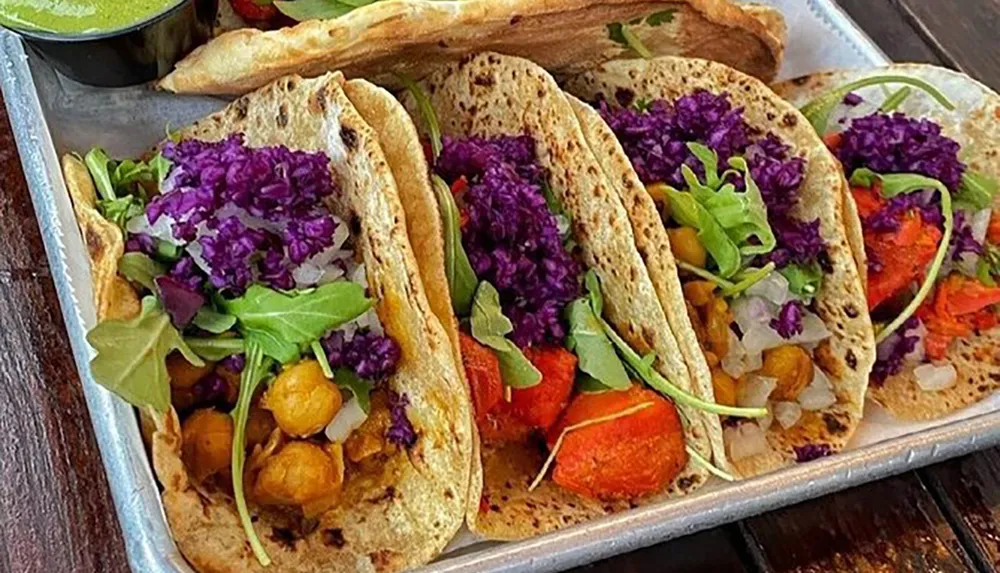 A tray contains three vibrant vegetarian tacos filled with purple cabbage greens diced onions and roasted vegetables