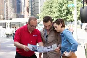 Three people are attentively examining a map or brochure on a city street.