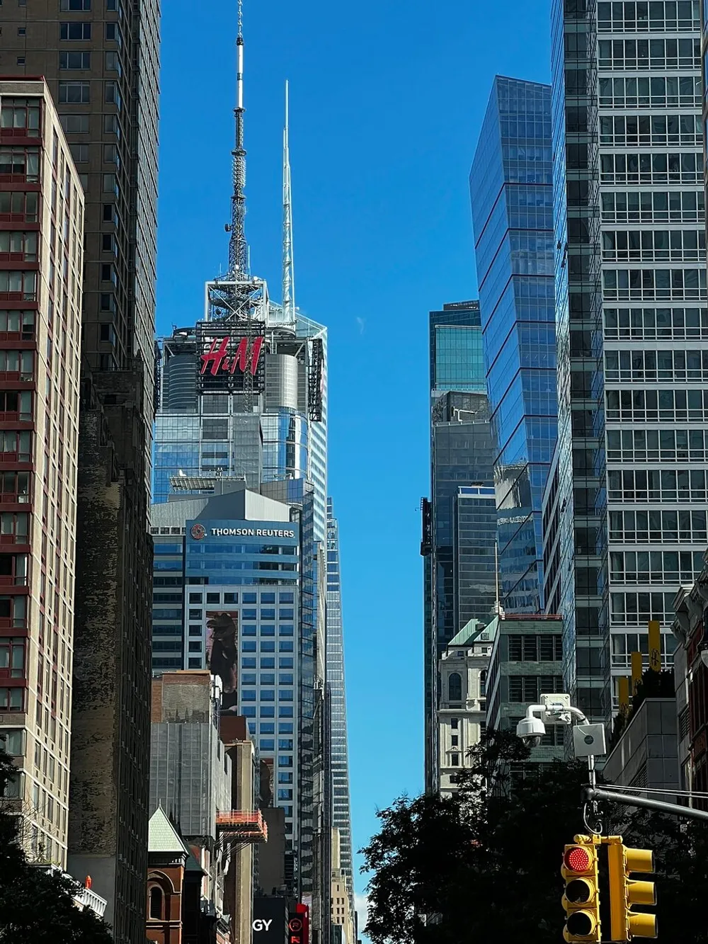 The image showcases a clear day in a bustling city with tall skyscrapers including one with the HM logo and a traffic light in the foreground displaying a red stop signal