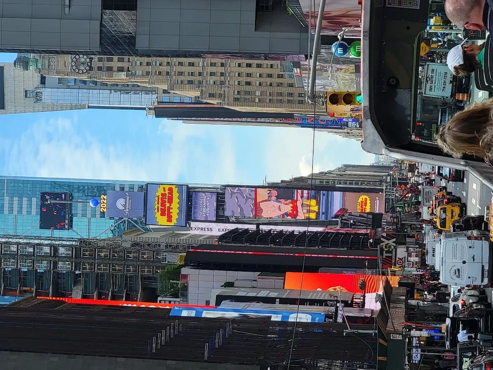 The image shows a bustling urban street scene with bright electronic billboards and signs captured in daylight and rotated 90 degrees to the right