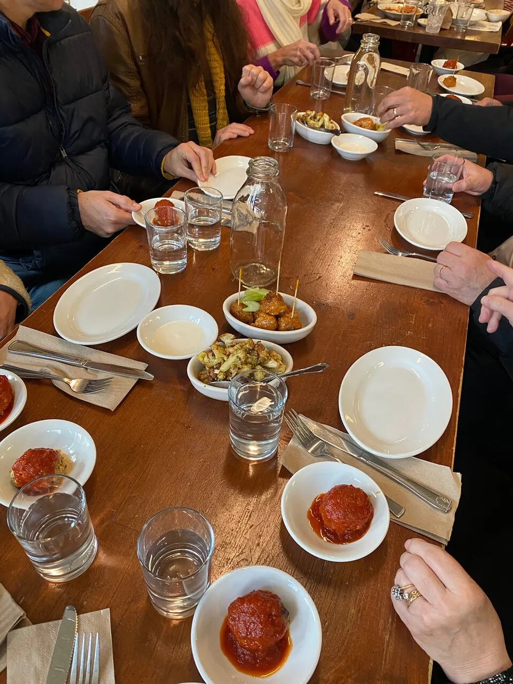A group of individuals is gathered around a table enjoying a meal with various dishes including what appears to be meatballs and glasses of water