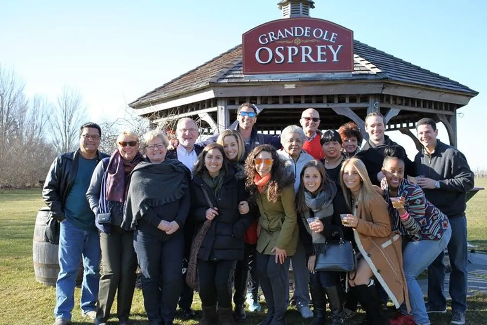 A group of smiling people is posing for a photo in front of a structure with a sign that reads GRANDE OLE OSPREY