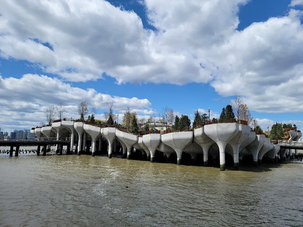 The image displays an architecturally unique undulating waterfront structure with concrete supports resembling a series of interconnected domes under a partly cloudy sky