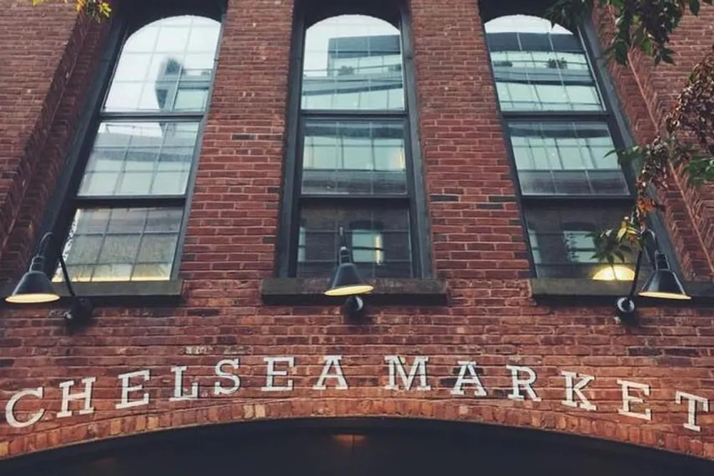 The image displays the exterior of the Chelsea Market with its name in large letters on a brick facade flanked by overhead lights