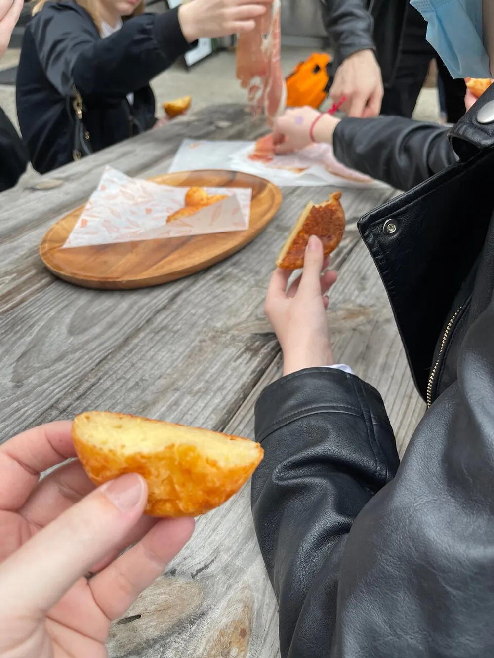 People are sharing and enjoying various fried foods at an outdoor wooden table