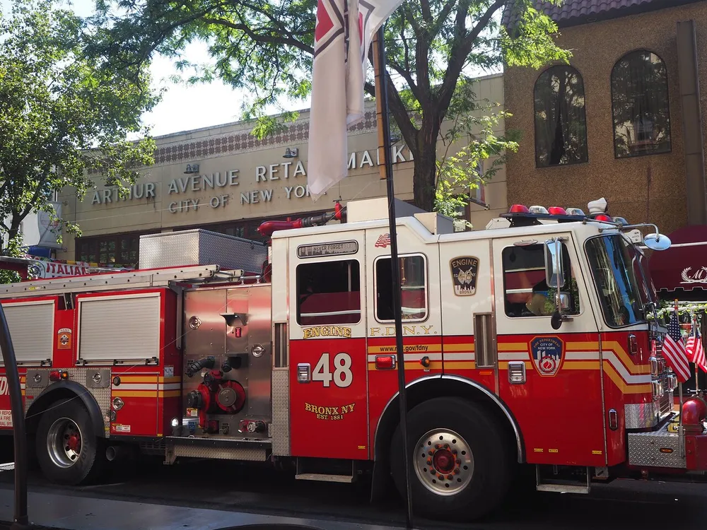 A New York City Fire Department FDNY fire engine marked with Engine 48 is parked on a city street in front of the Arthur Avenue Retail Market