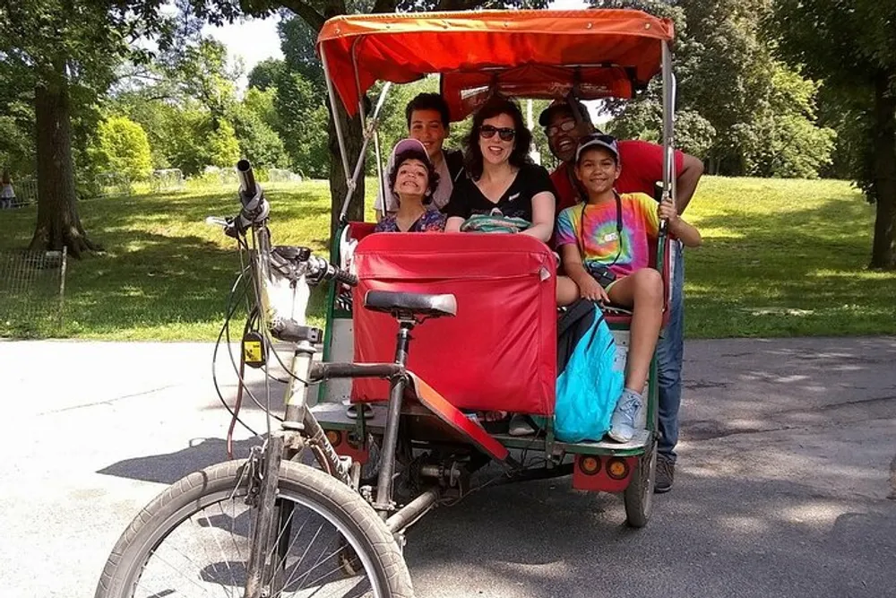 A group of people is smiling for the camera while seated in a red canopy-covered cycle rickshaw in a park setting
