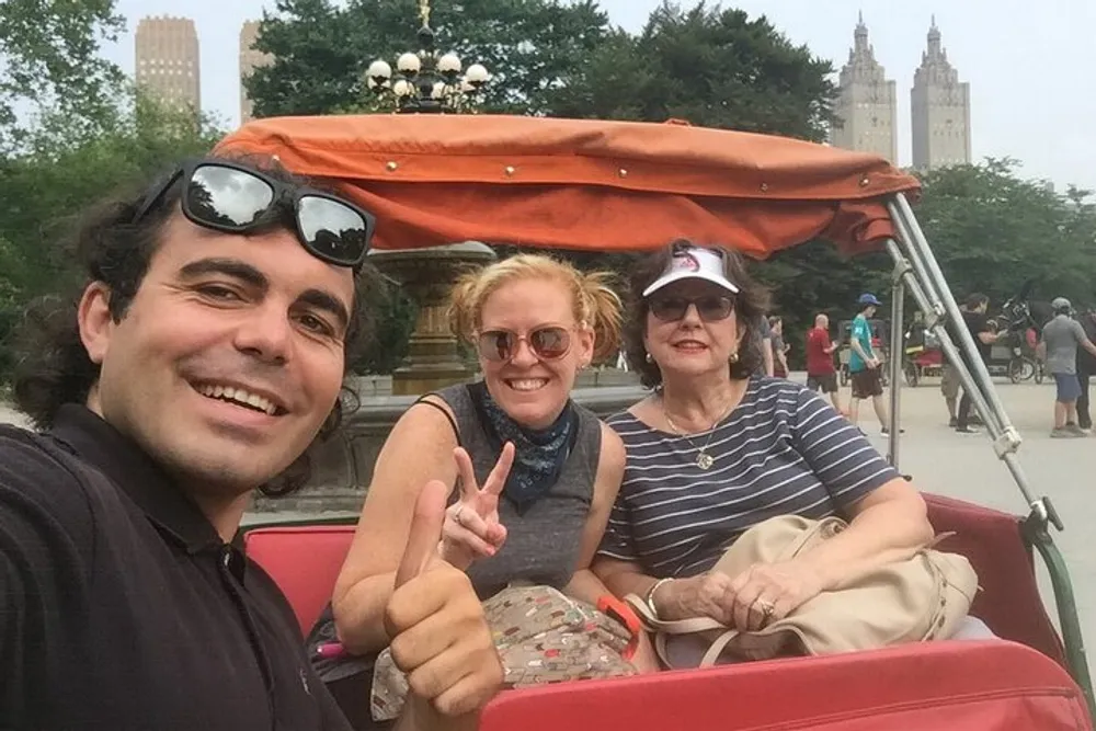 Three people are posing for a happy selfie while seated in a pedicab with people and buildings visible in the background