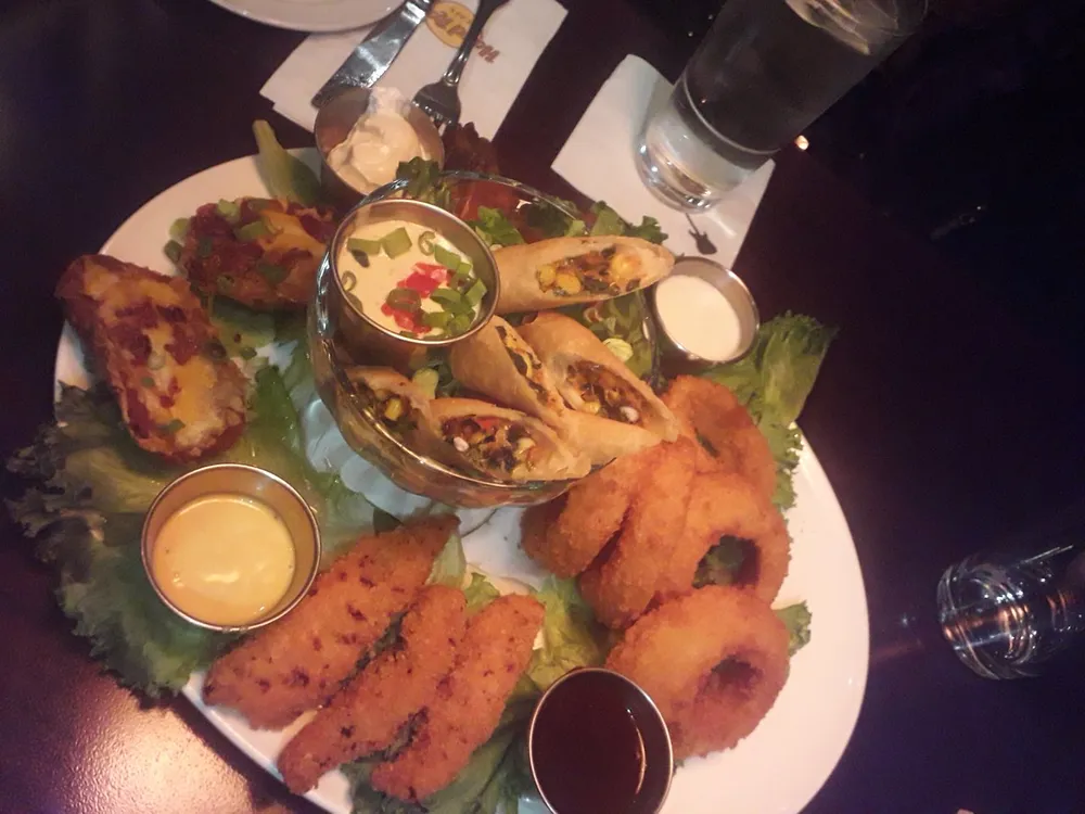 The image shows a plate of assorted appetizers including items like loaded potato skins chicken tenders and onion rings served with variety of dipping sauces on a restaurant table