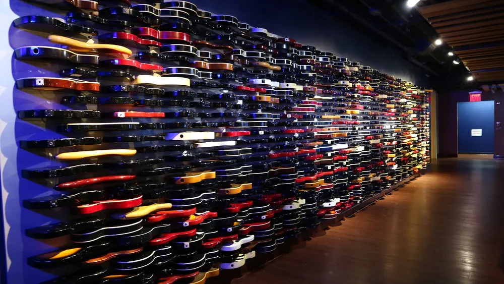 The image displays an impressive wall adorned with a multitude of colorful electric guitars creating a vibrant and artistic installation