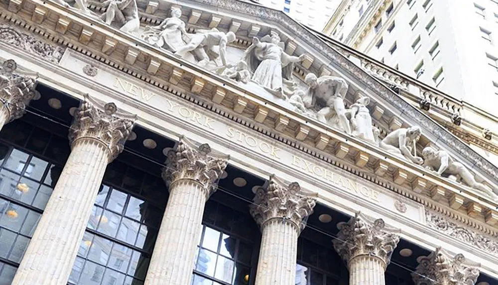 The image shows the ornate neoclassical facade of the New York Stock Exchange building with its distinctive Corinthian columns and sculptural figures above the entrance