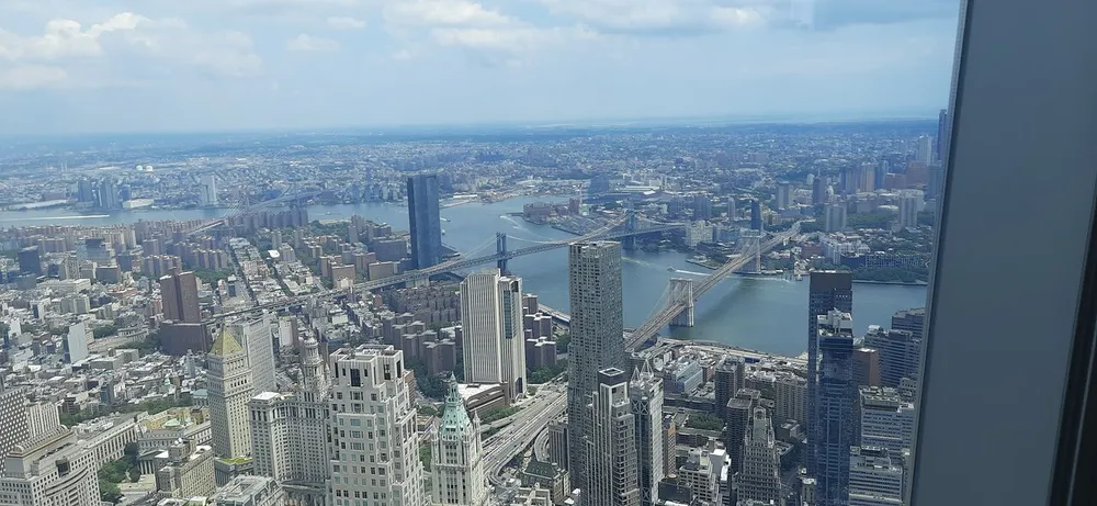 The image shows an aerial view of a dense urban skyline with multiple skyscrapers and two bridges spanning a wide river captured from a high vantage point