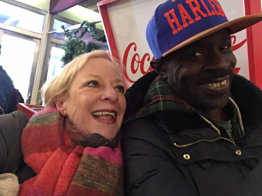 A smiling man and woman are closely posing for a selfie appearing joyful and casually dressed with a Coca-Cola advertisement in the background