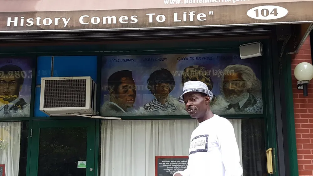 A man in a white hat stands in front of a storefront with a mural featuring historical figures and the phrase History Comes To Life