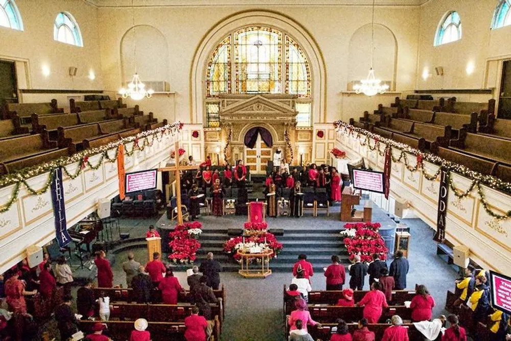 The image depicts a church congregation with many individuals dressed in red garments during a service with Christmas decorations adorning the interior