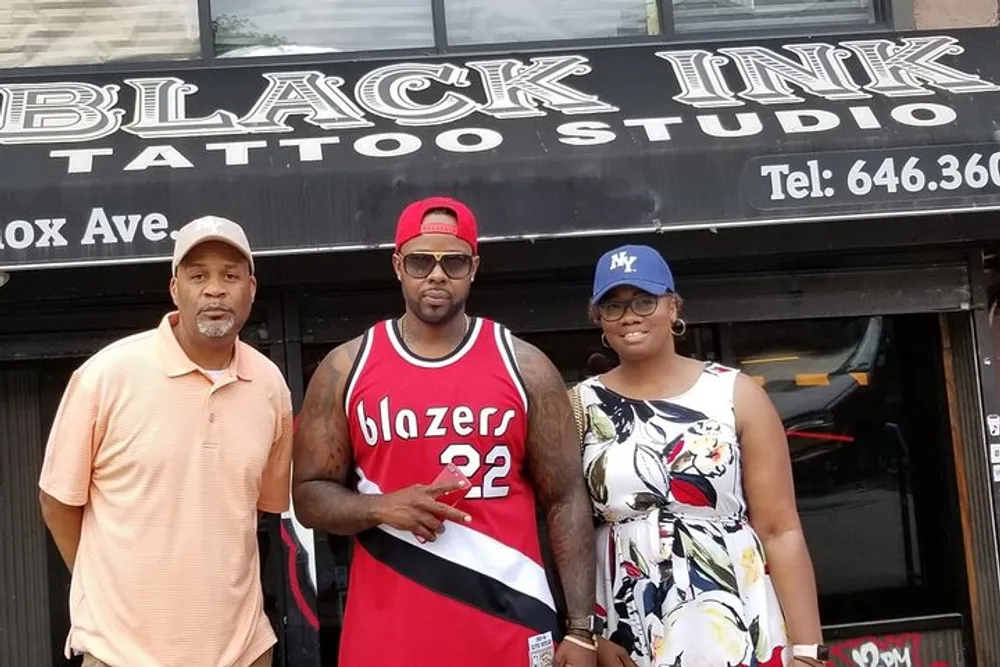 Three people are posing in front of the BLACK INK TATTOO STUDIO storefront
