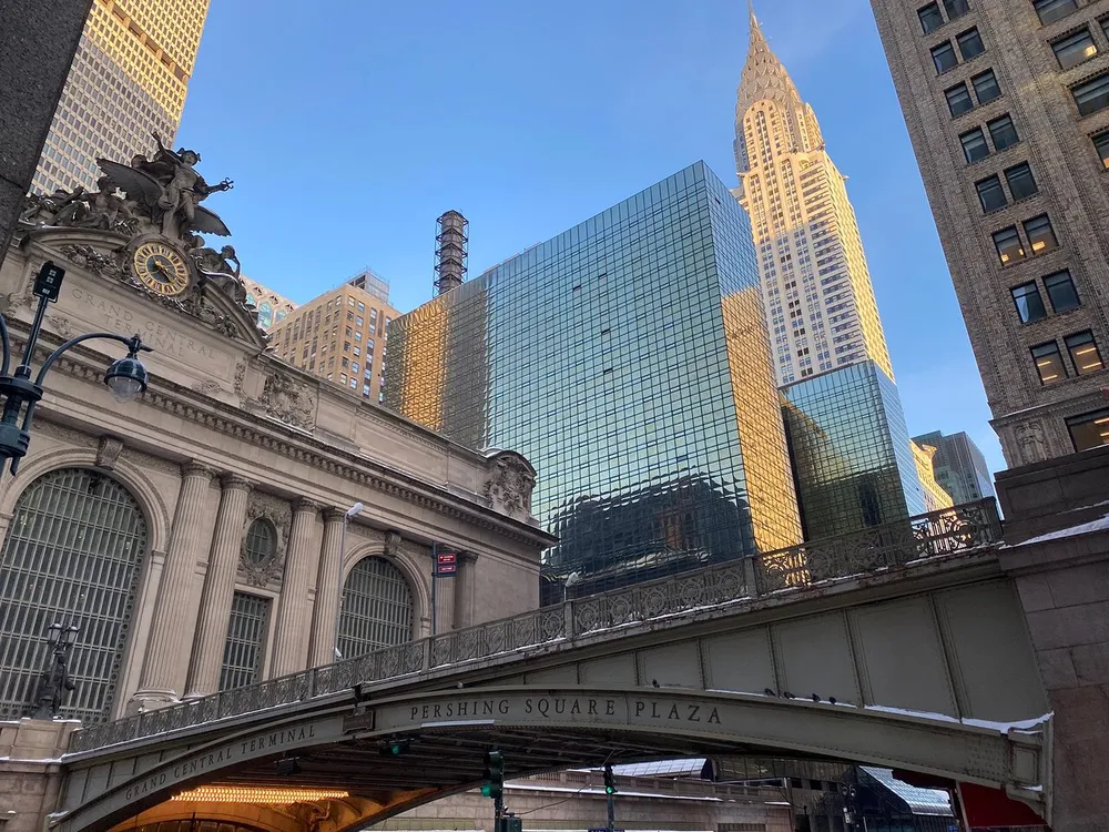The image captures a juxtaposition of the classic architecture of Grand Central Terminal against the modern skyscrapers including the Chrysler Building in the heart of Midtown Manhattan
