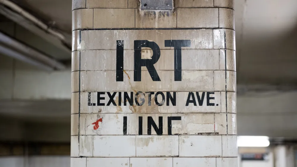 The image shows a worn and tiled column with the black lettering IRT Lexington Ave Line indicating a subway line designation