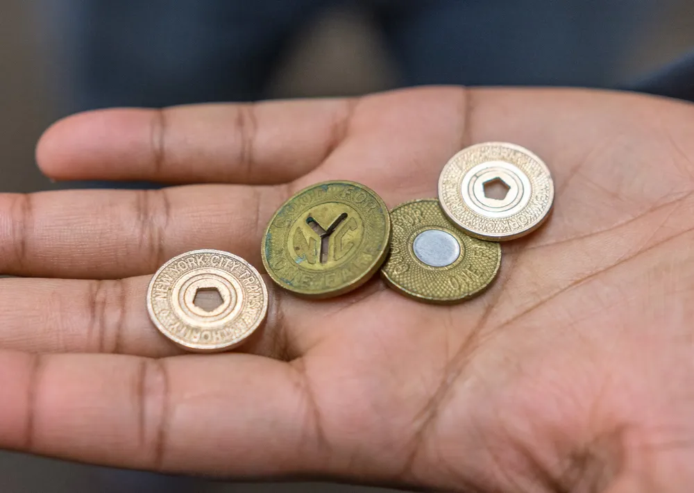 A persons open hand displays a collection of New York City transit tokens of different designs