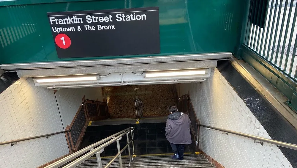 A person is descending the stairs into the Franklin Street Station entrance for uptown and the Bronx trains in the New York City subway system