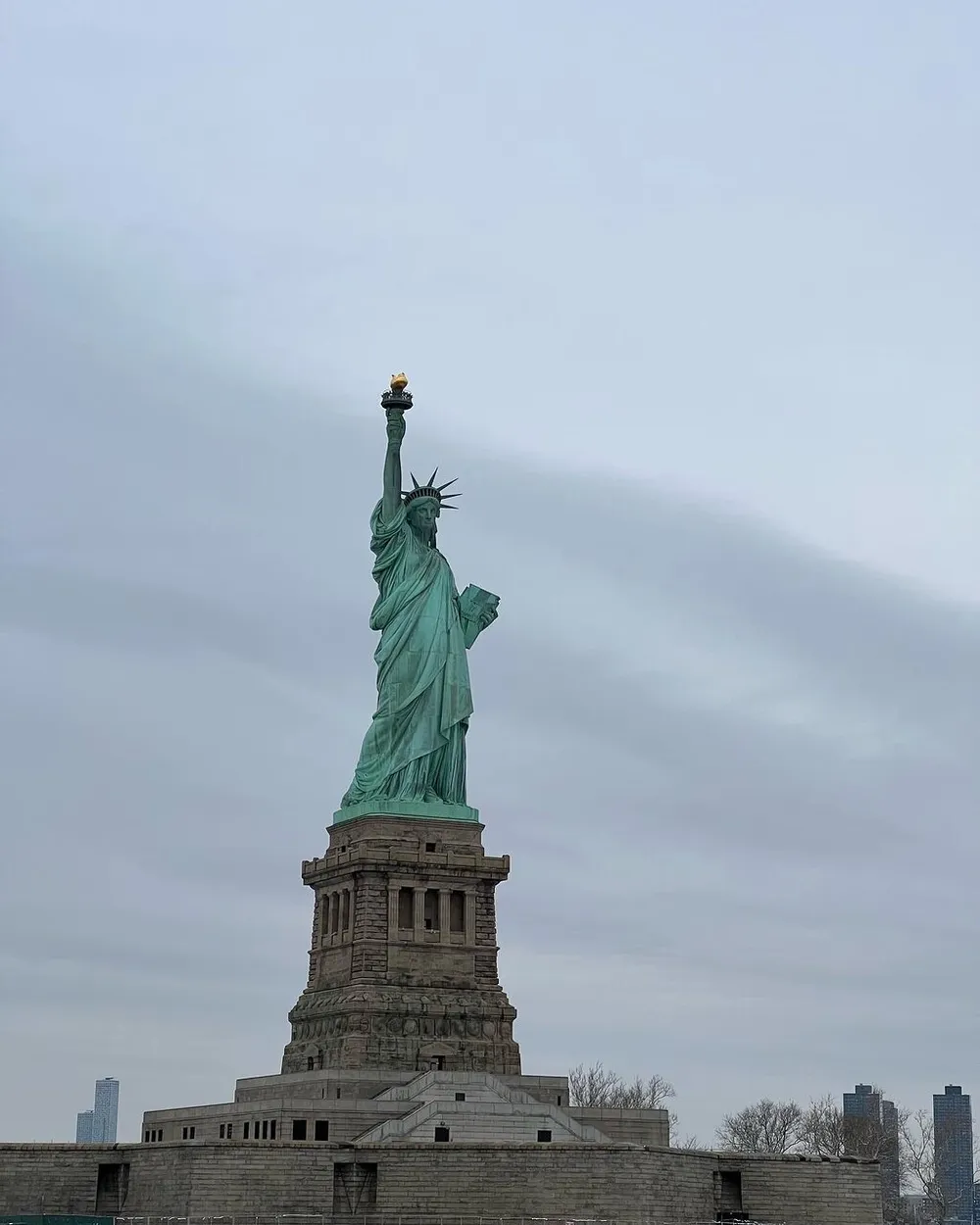 The image shows the Statue of Liberty standing tall against a cloudy sky