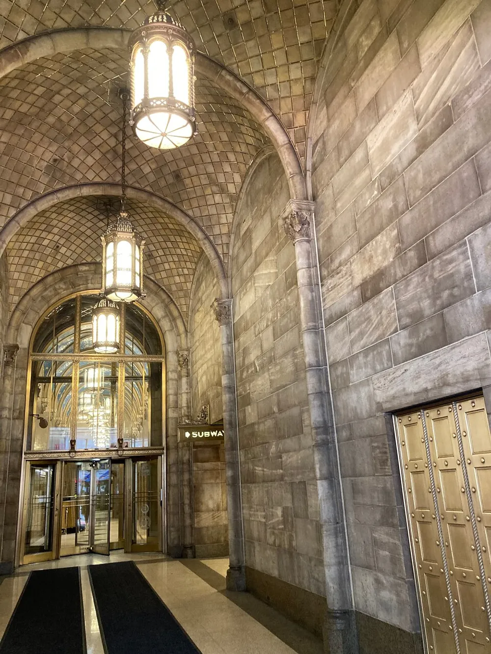 This image displays an elegant vaulted hallway with an arched ceiling ornate hanging lanterns and a sign indicating the entrance to a subway reflecting a blend of classic architectural grandeur with urban functionality