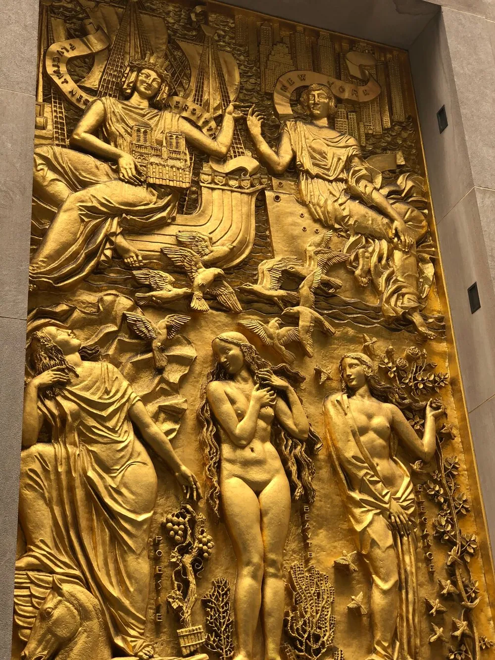 The image shows a detailed golden relief with allegorical figures architectural elements and various symbols evoking themes of classical antiquity and mythology