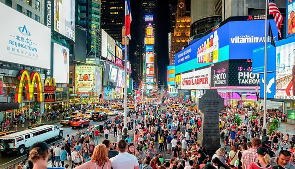 This image shows a bustling Times Square in New York City with large crowds of people bright neon billboards and traffic epitomizing the vibrancy and energy of an iconic urban center