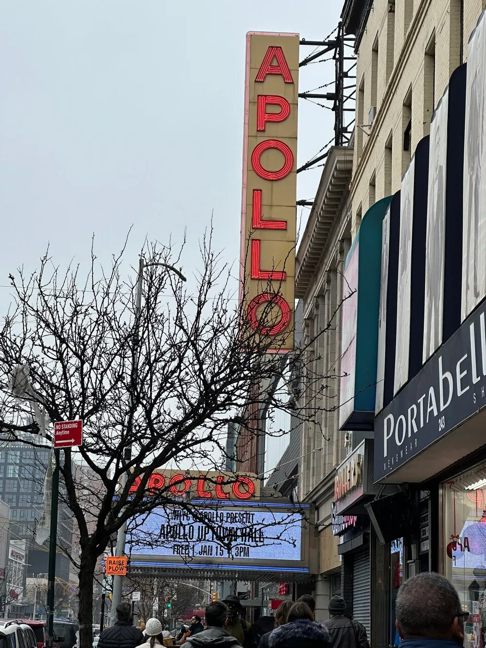 This image shows people walking by the iconic Apollo Theater marquee with neon signage in an urban setting