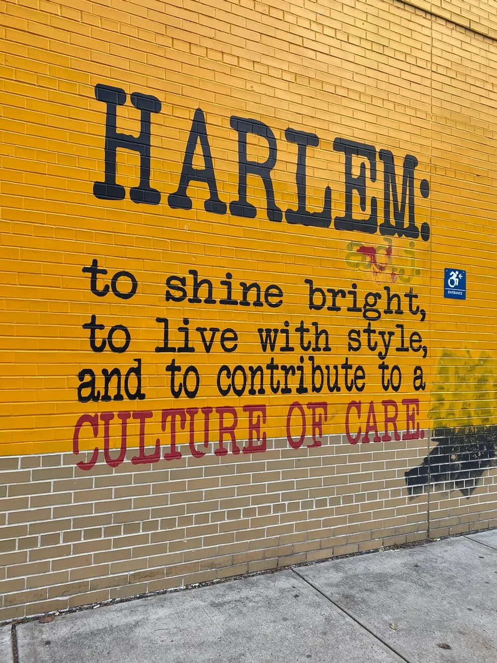 The image shows a yellow brick wall with large black letters spelling HARLEM along with a motivational message in smaller black and red letters below endorsing a culture of care