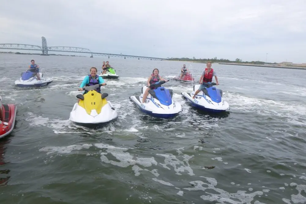 A group of people is riding jet skis on a body of water with a bridge in the distant background