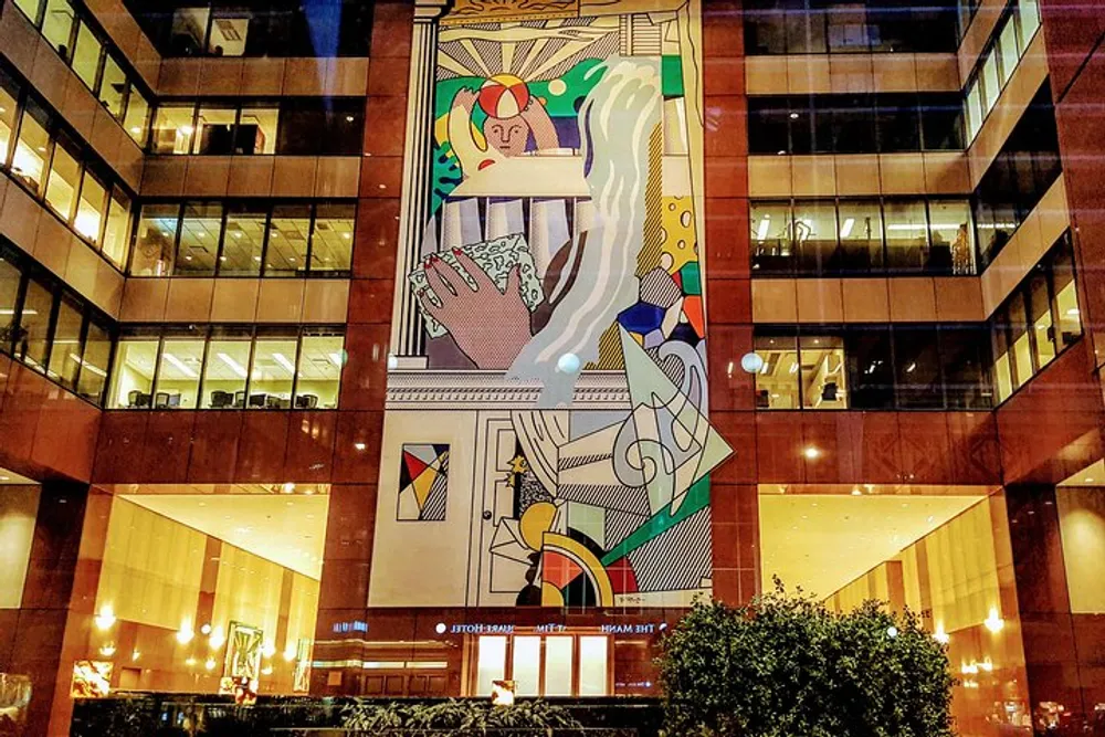 The image shows a colorful mural with abstract and figurative elements displayed on a buildings facade at night accentuated by indoor lighting